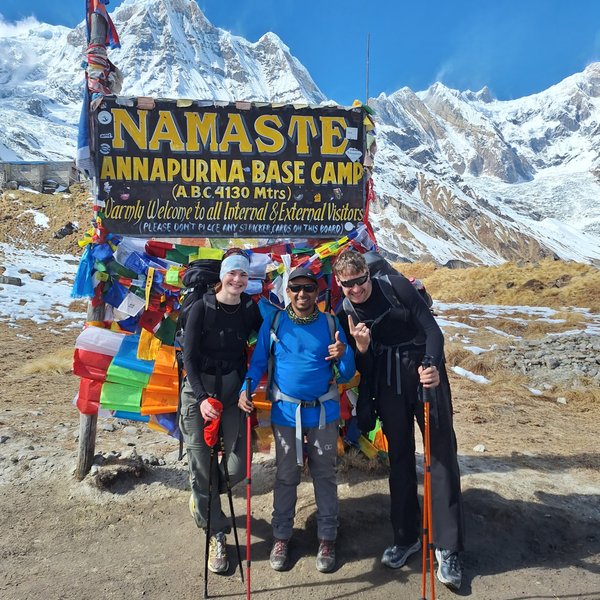 Trekkers at Annapurna Base Camp with colorful prayer flags and Himalayan mountains 	