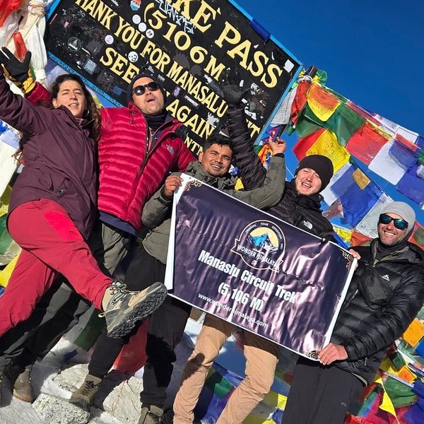 Happy trekkers celebrating beside Buddhist prayer flags during the Manaslu Circuit Trek in Nepal