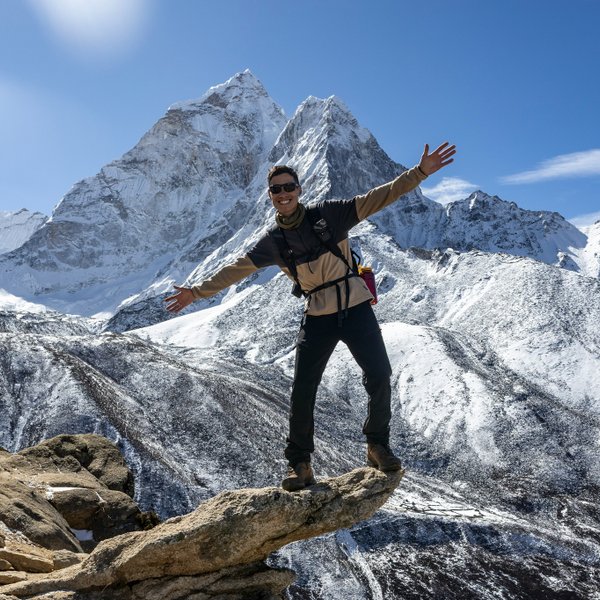 Trekker celebrating with arms raised on a rocky summit, Everest Base Camp Trek, Nepal