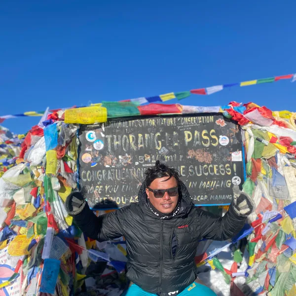 Trekker resting beside the Thorong La Pass 5,416m signboard surrounded by colourful prayer flags