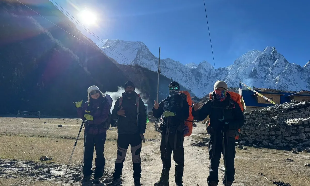Hikers with backpacks and trekking poles pose in front of snow-capped mountains.