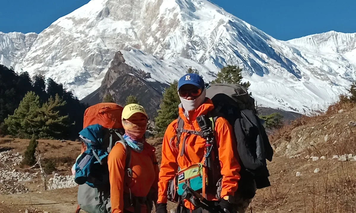 Hikers with large backpacks stand before a majestic snow-capped mountain under a clear blue sky.