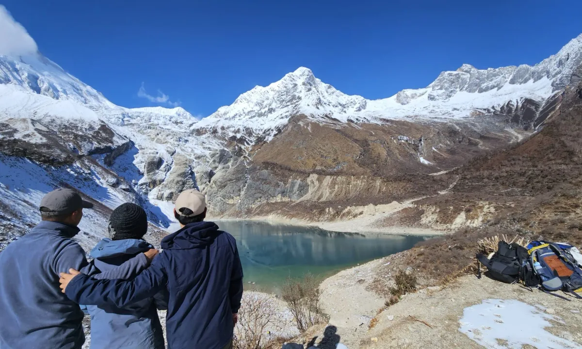 Three hikers admire a serene, turquoise lake surrounded by snow-capped mountains.