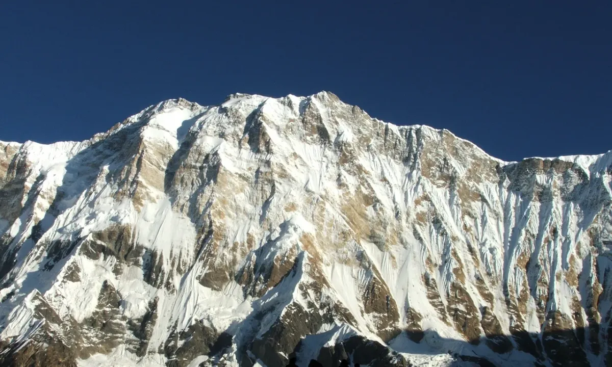 Hikers silhouetted against a massive snow-capped mountain under a deep blue sky.