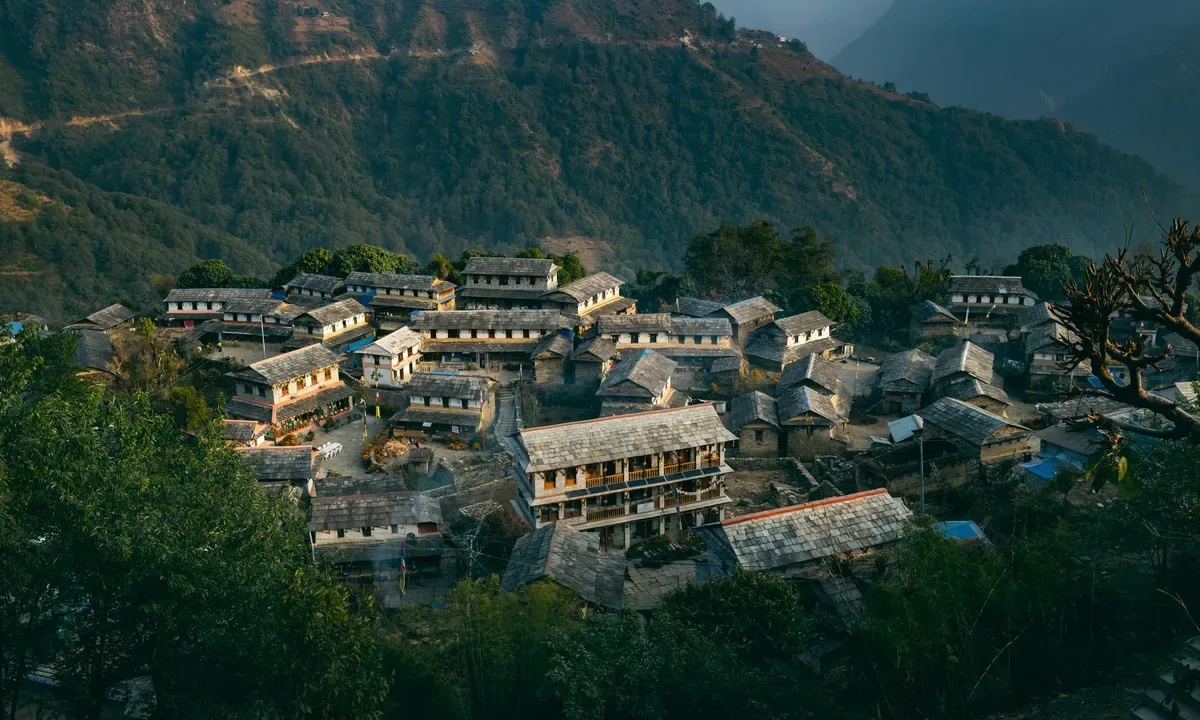 Village nestled in a lush green mountain landscape, with traditional stone houses.