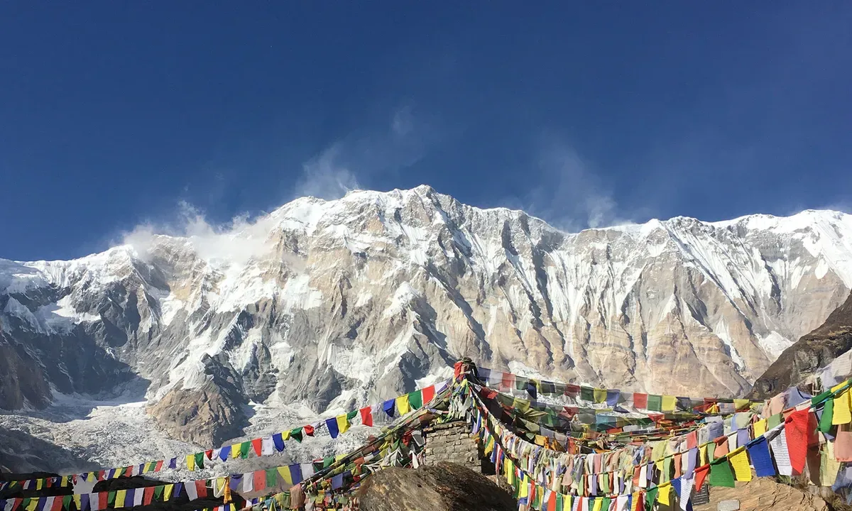 Prayer flags flutter before snow-capped Annapurna mountain range in Nepal.
