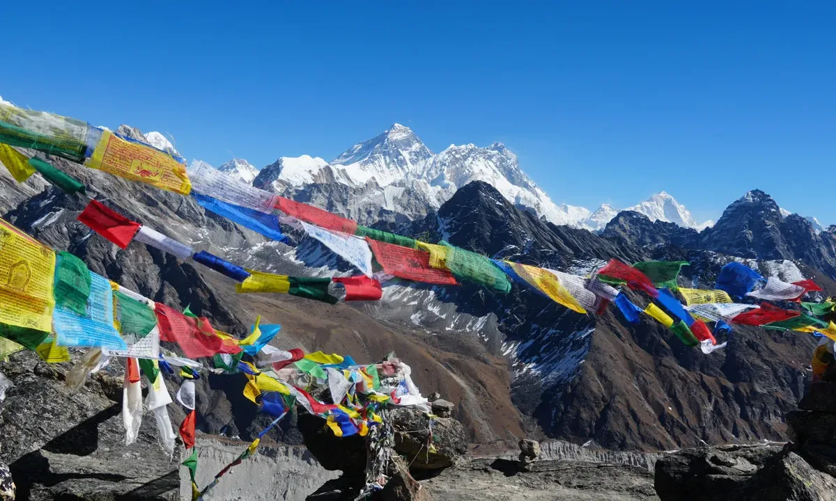 Prayer flags flutter against a backdrop of snow-capped Himalayan peaks.