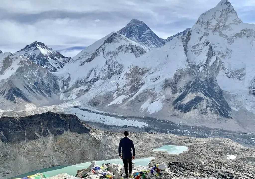 Man overlooking Everest, glacial lakes, and prayer flags.