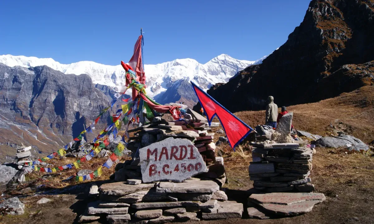 Mardi Himal Base Camp sign at 4500m with colorful prayer flags and snow-capped Himalayas in the background