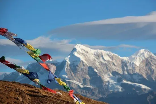 Traditional Buddhist prayer flags blowing in wind with majestic Himalayan mountain range and clouds on Pikey Peak Trek route