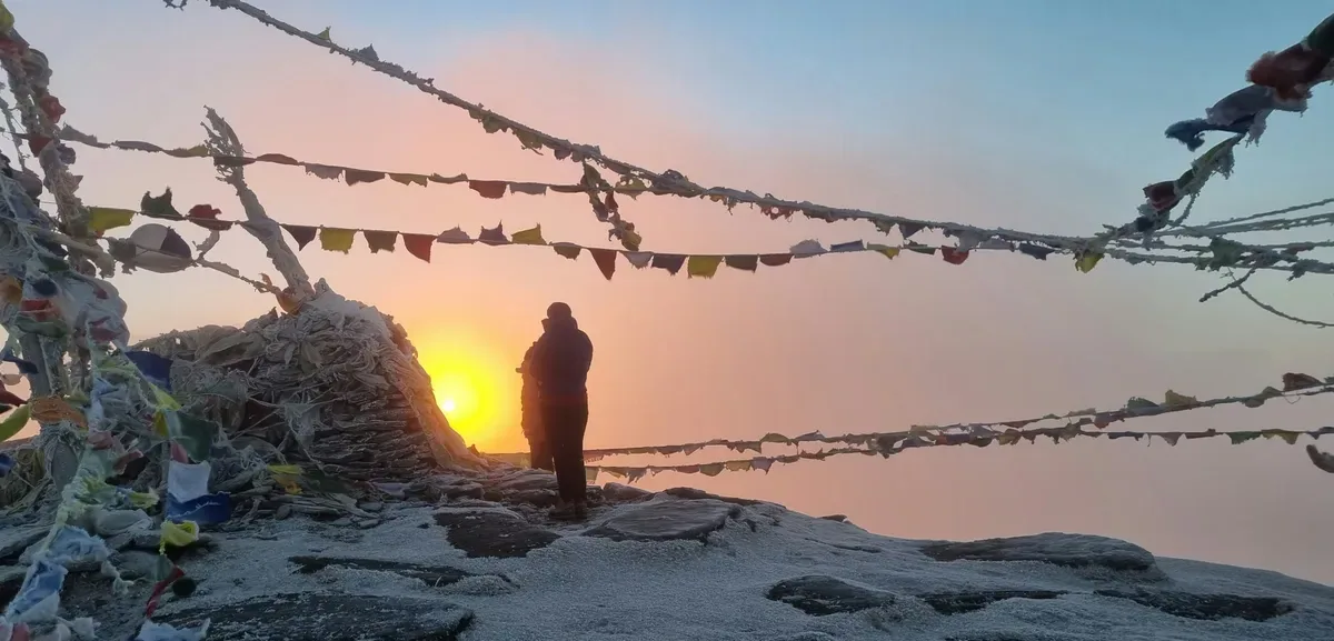 Silhouette of trekker at golden sunset with prayer flags and Himalayan horizon on Pikey Peak Trek, eastern Nepal