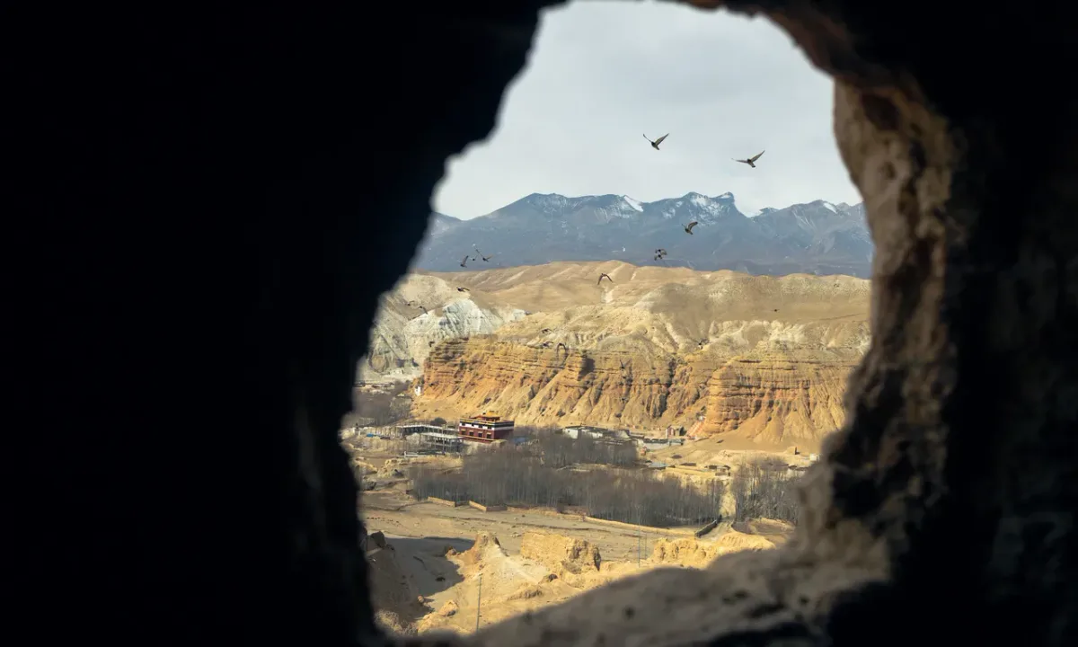 View through ancient cave entrance overlooking vast canyon landscape and arid valleys of Upper Mustang, Nepal