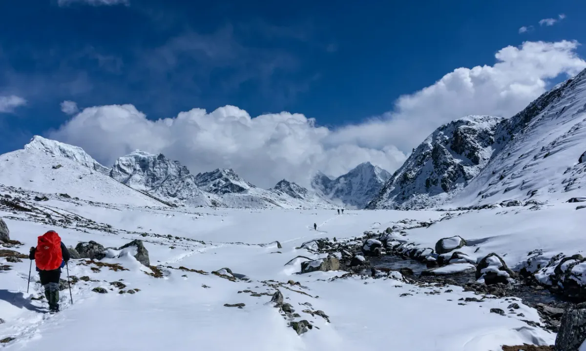 Trekker crossing Cho La Pass in winter snow with dramatic Himalayan mountain backdrop, Everest Three Passes Trek Nepal