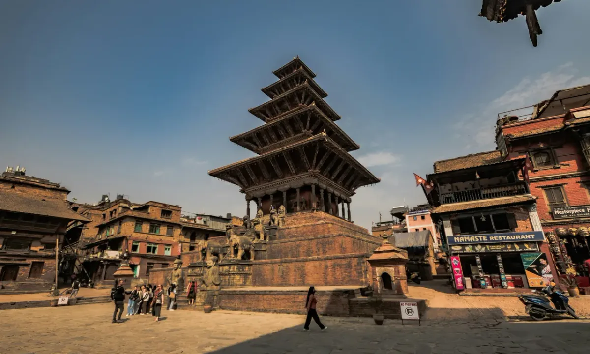 A wide-angle view of the five-story Nyatapola Temple in Bhaktapur, Nepal, showing its towering pagoda structure and the stone guardians lining its steep central staircase.