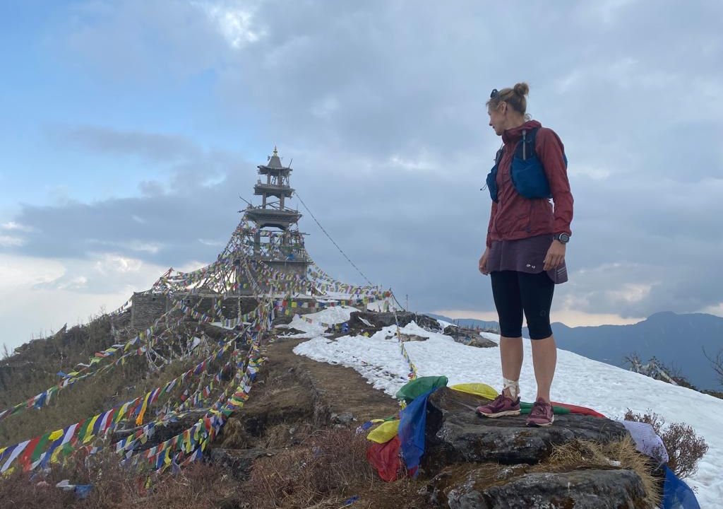 Trail runner standing at Ama Yangri Peak summit with snow and prayer flag monastery Nepal