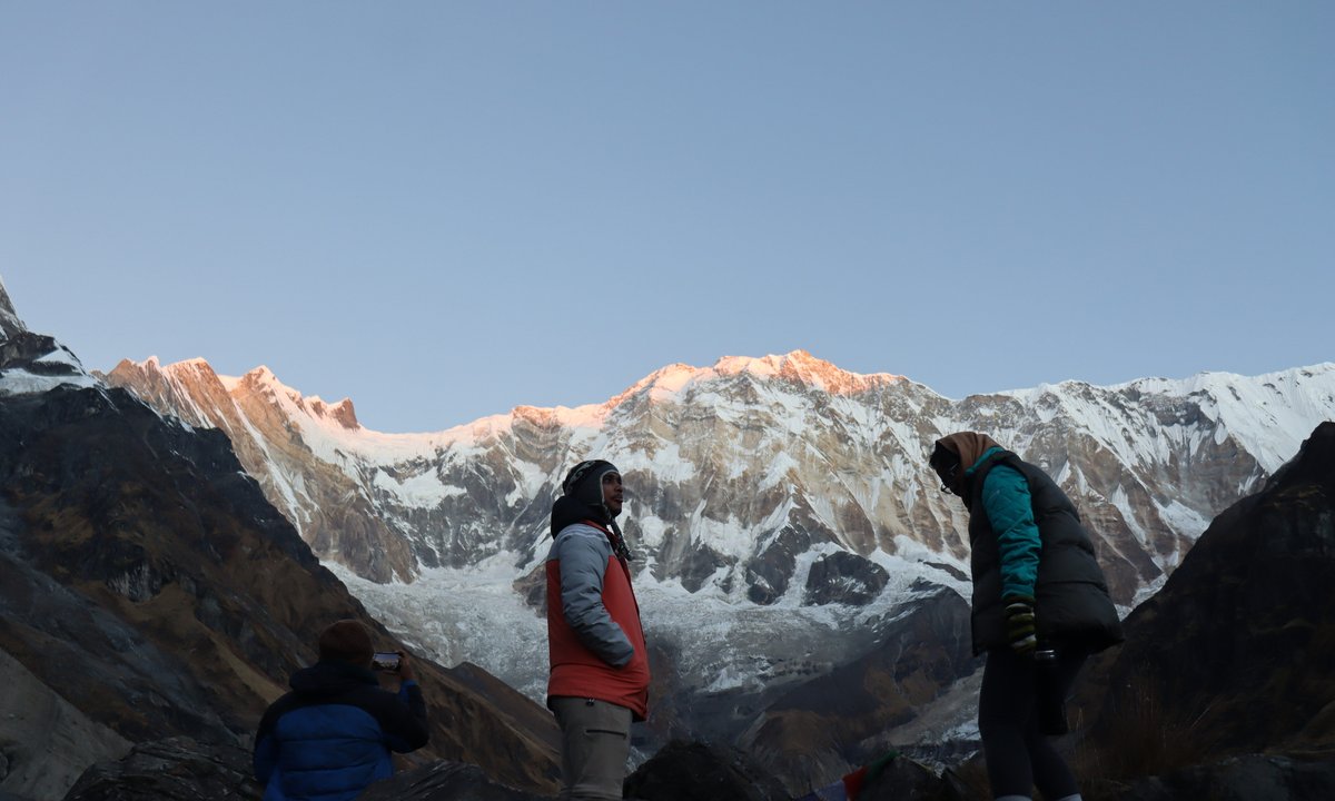 Trekker standing at Annapurna Base Camp at sunrise with towering snow peaks behind, Nepal