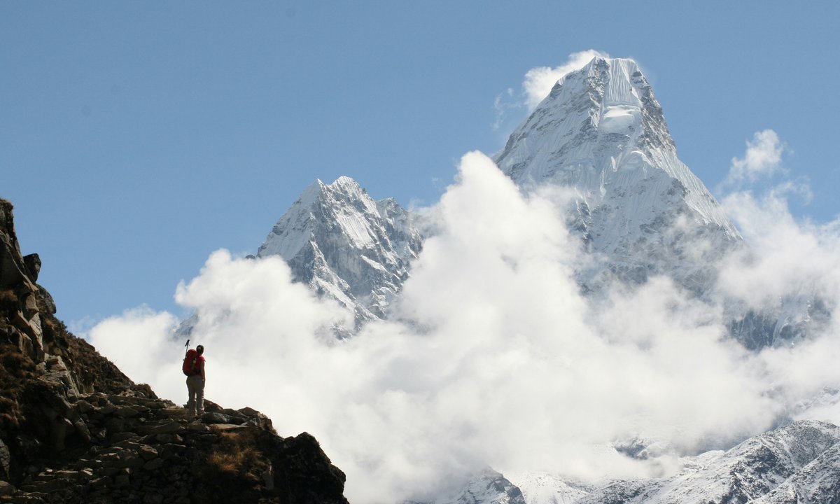 Trekker on ridge, Ama Dablam in clouds behind  Trekker on rocky ridge with Ama Dablam 6812m rising above clouds on Everest Base Camp Trek Nepal