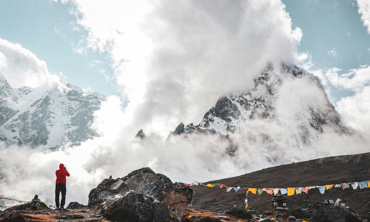 Red jacket trekker, prayer flags, Everest and Lhotse massif in cloud  Trekker in red jacket near prayer flags with Everest Lhotse massif in cloud Khumbu region Nepal