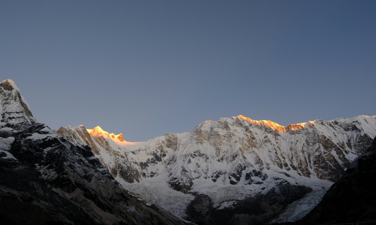 Sunrise over Annapurna Sanctuary, golden light striking snow peaks above a shadowed valley