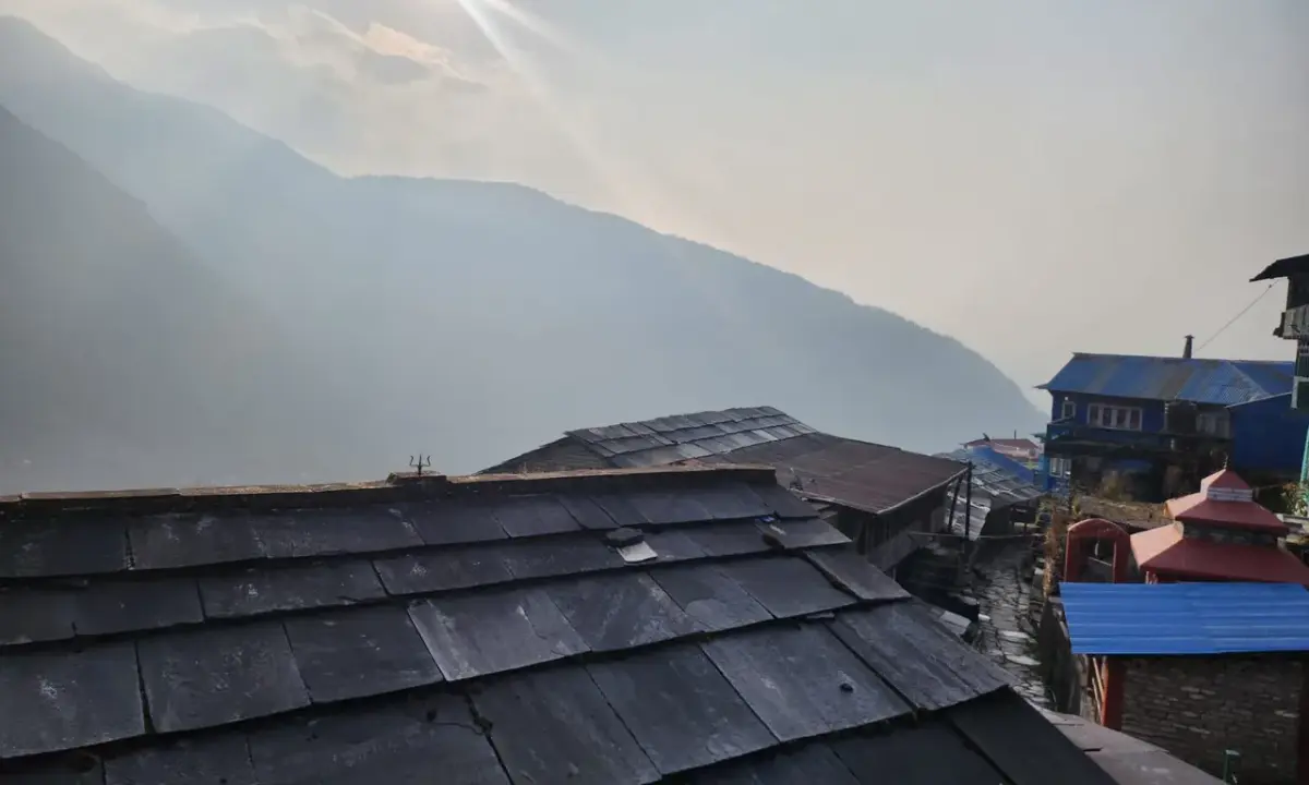 Traditional stone slate rooftops of Ulleri village with misty mountains and morning sunlight in background, Annapurna foothills Nepal
