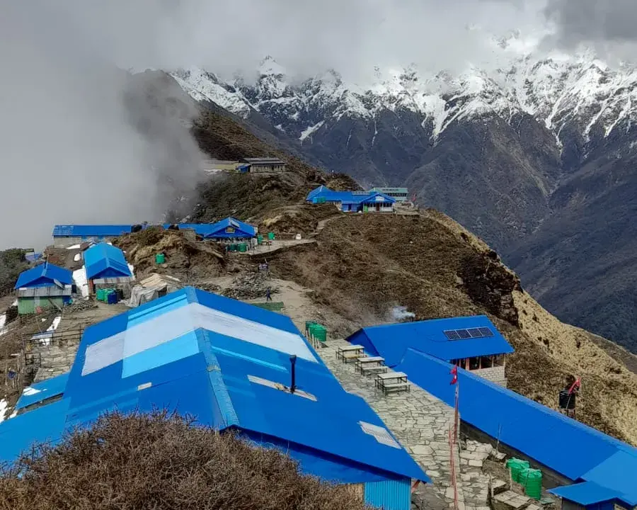High Camp — the cluster of blue-roofed teahouses perched on the ridge, with the Annapurna range behind the clouds.
