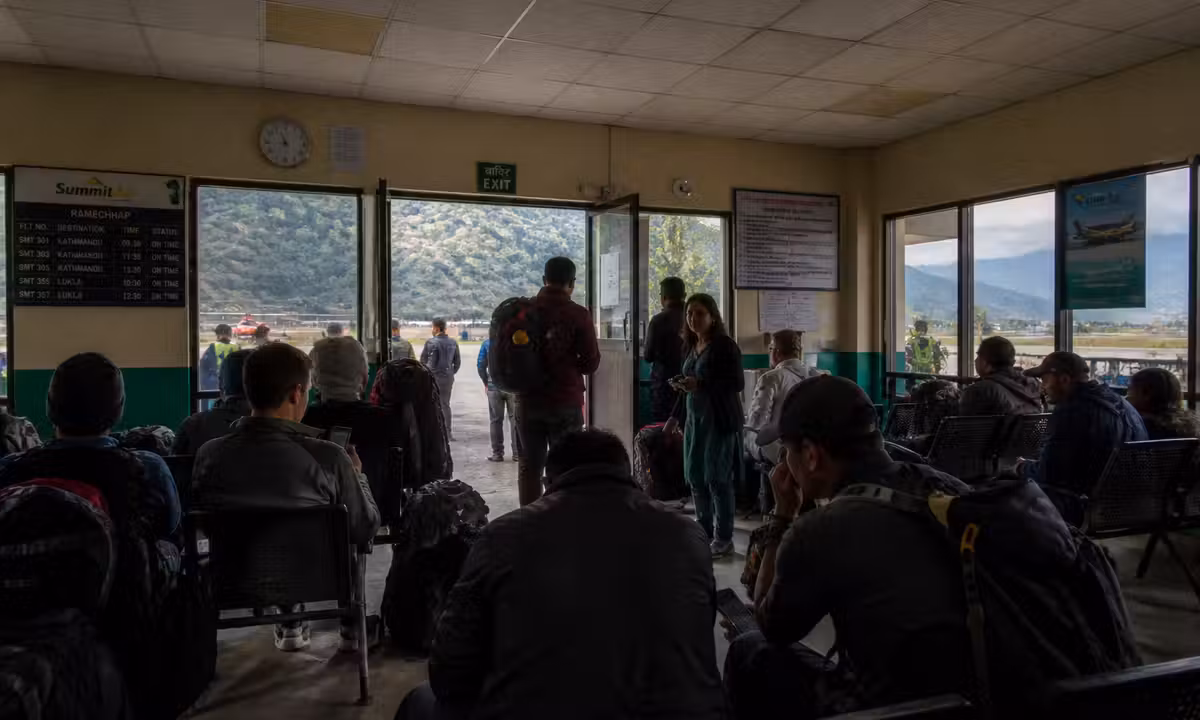 Travellers waiting at Ramechhap airport in Nepal with overcast skies and mountains in the background