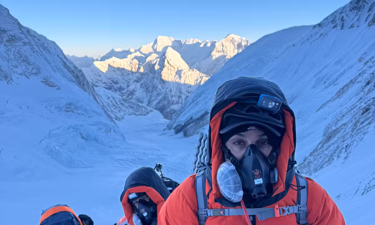 Sudhigya Pant in a red high-altitude jacket and oxygen mask during the Everest summit push, with snow-covered Himalayan peaks stretching behind him