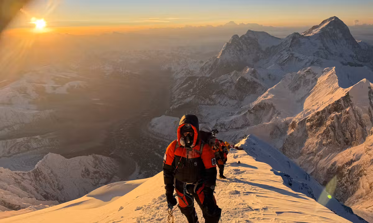 Sudhigya Pant and his team climbing Everest's upper ridge at sunrise, with a sweeping golden panorama of the Himalayas below