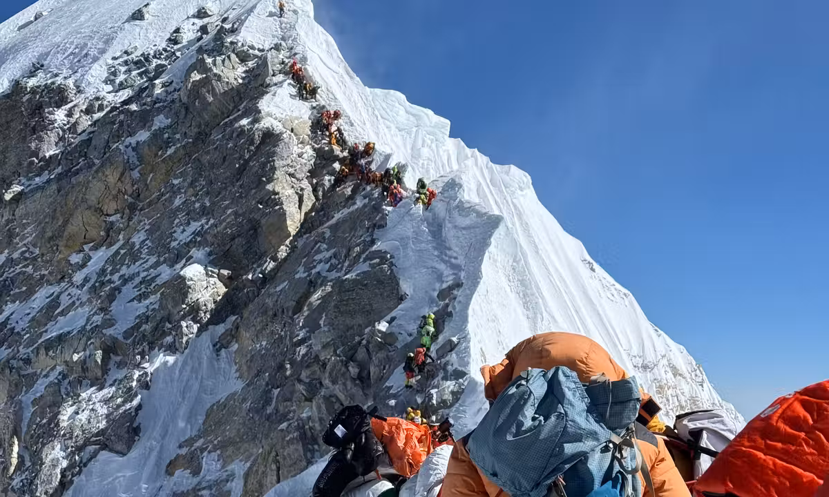 A long line of climbers queuing on a near-vertical section of Everest's upper route, showing the traffic and exposure on the world's highest mountain