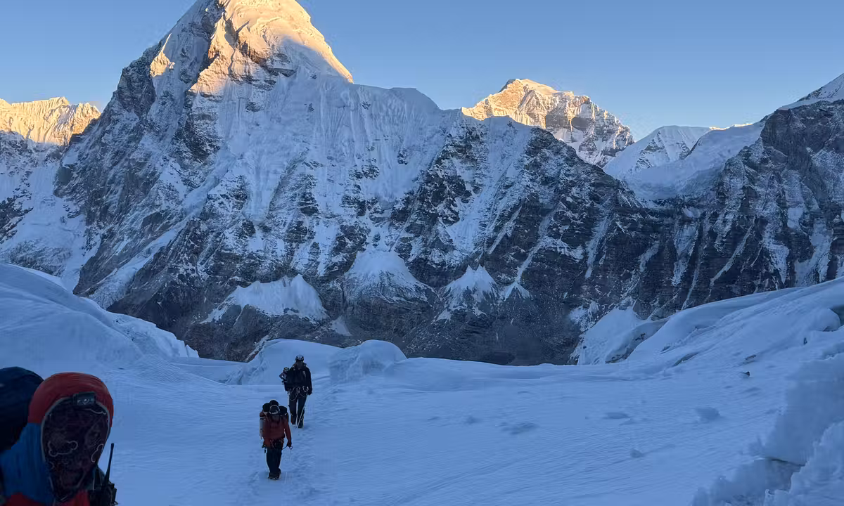 Two climbers crossing the Khumbu Glacier with towering Himalayan peaks lit by early morning alpenglow — Everest expedition 2026