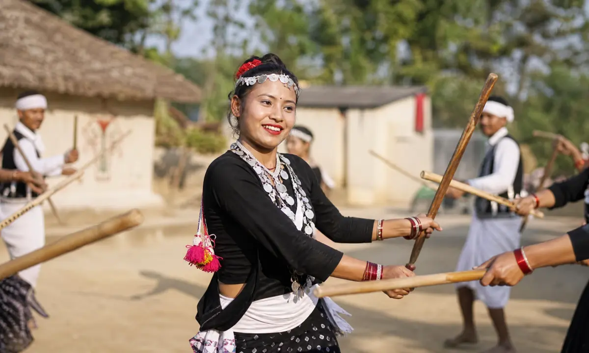 Tharu woman in traditional black-and-white costume performing Lathi Naach stick dance with bamboo poles at an outdoor cultural festival in Nepal
