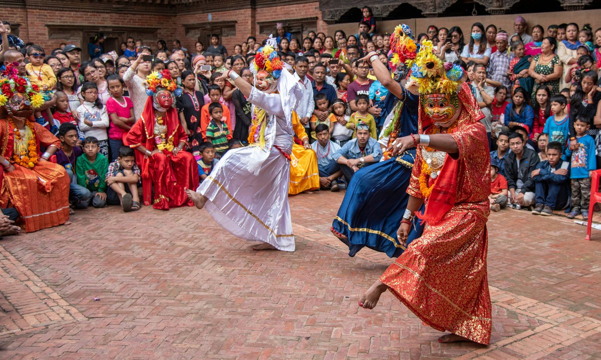Lakhey in colourful costumes with floral headdresses performing traditional Nepali folk dance before a large crowd in a temple courtyard in Nepal