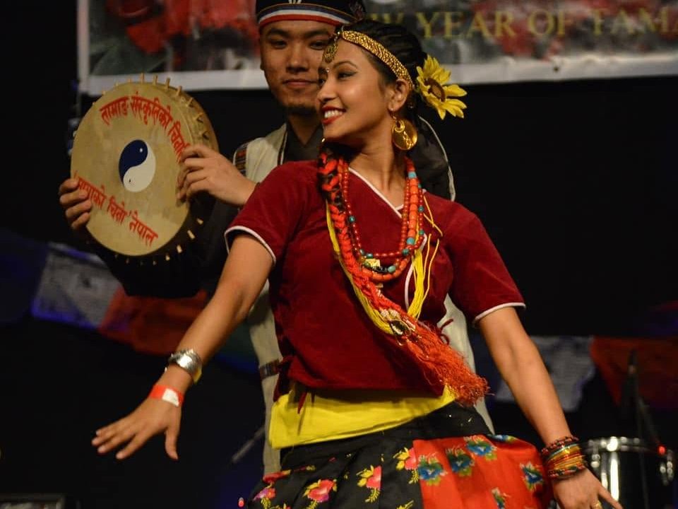 Tamang woman in traditional dress performing Tamang Selo dance with a damphu drum player behind her at a cultural event in Nepal