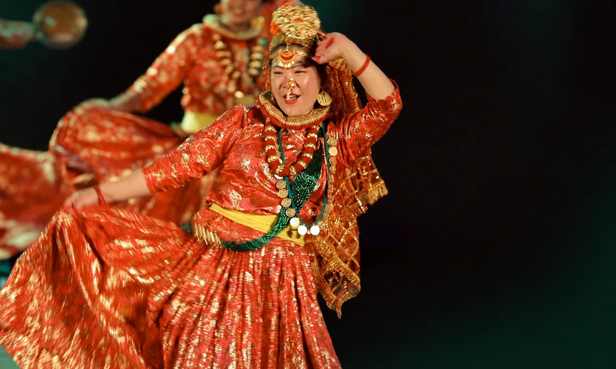 Nepali woman performing Maruni Dance in red and gold traditional costume performing a folk dance on stage, with swirling dress and heavy gold jewellery