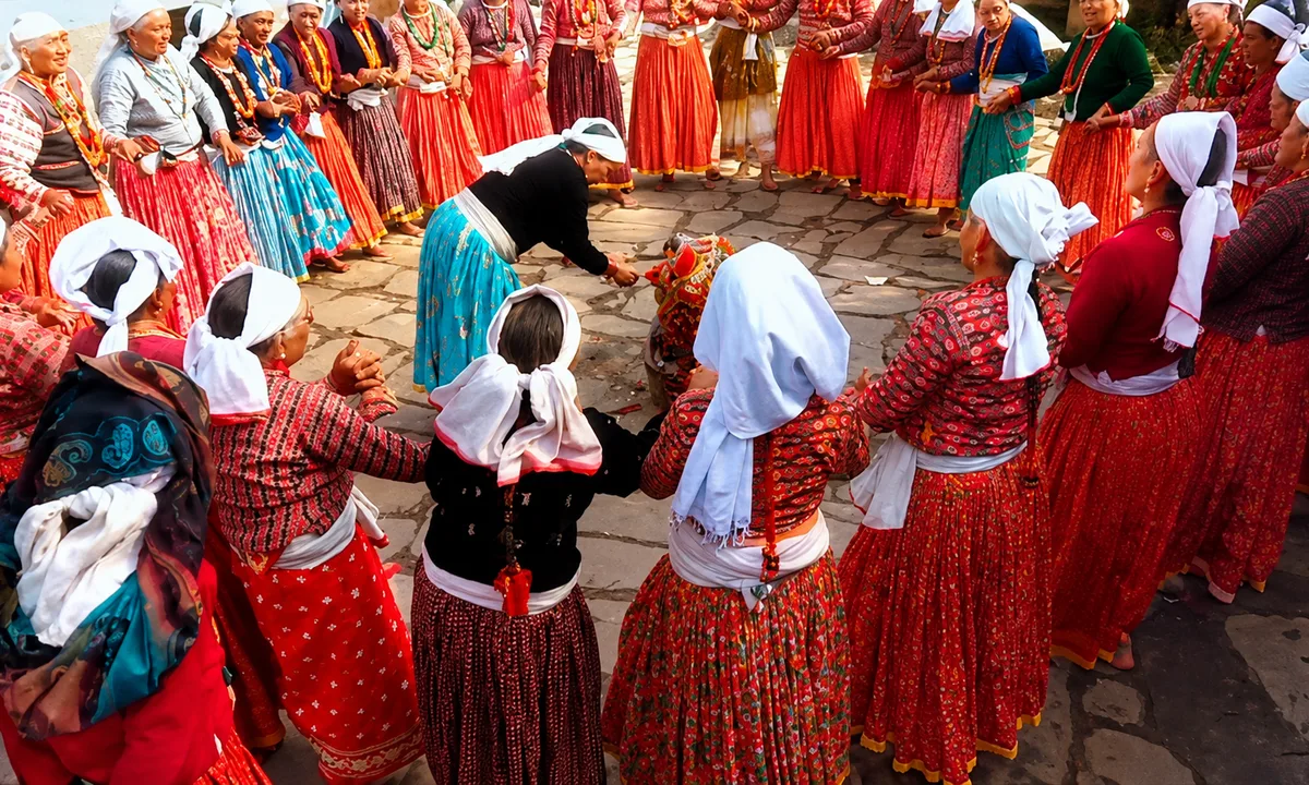 Women in traditional red Nepali hill community dress holding hands in a large circle deuda dance at an outdoor cultural gathering in Nepal