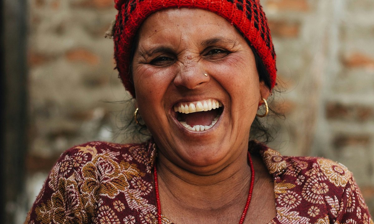 Nepali woman from the Bahun community laughing warmly, wearing traditional red headscarf and red bead necklace in Nepal