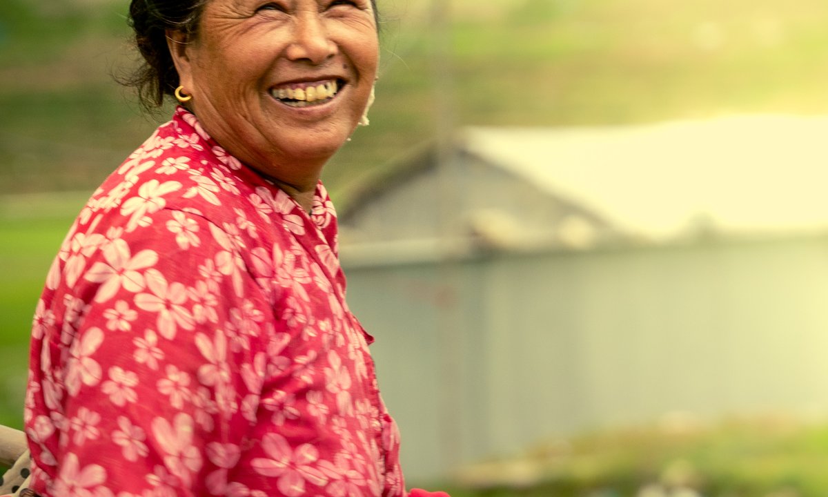 Smiling Nepali farmer woman in traditional red floral dress celebrating Rastriya Dhan Diwas in a rice field