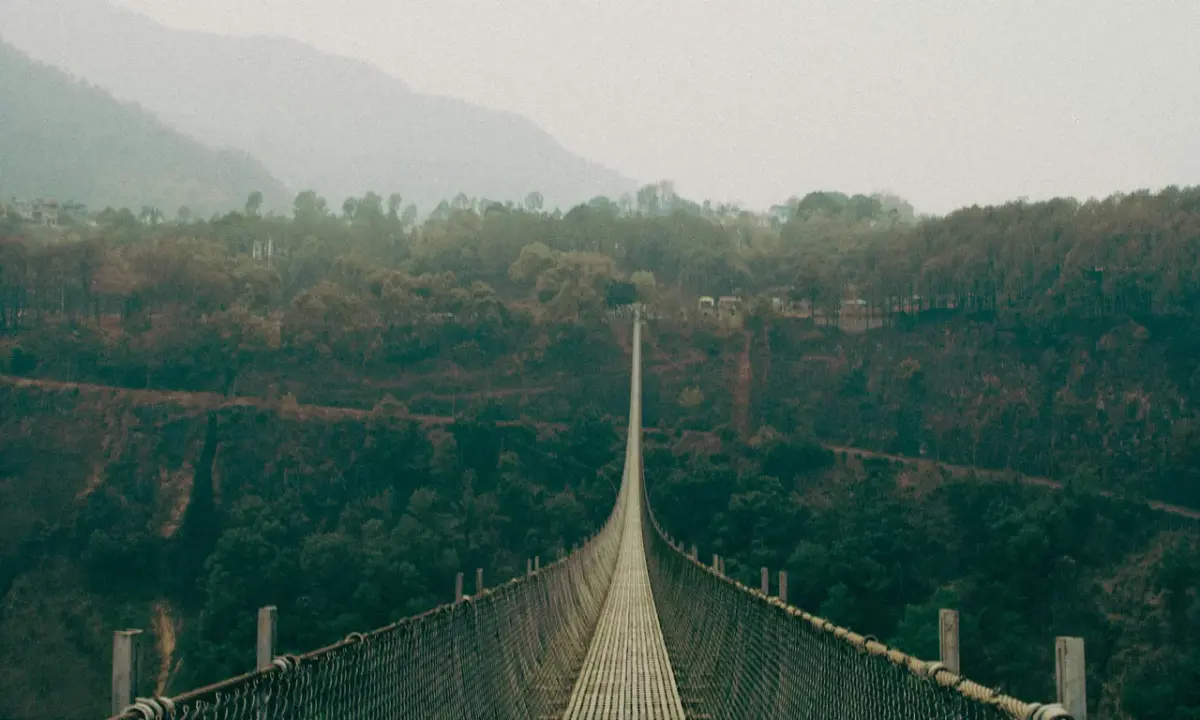Long suspension bridge stretching across a deep forested gorge in Baglung, Nepal, surrounded by misty green hills and autumn 