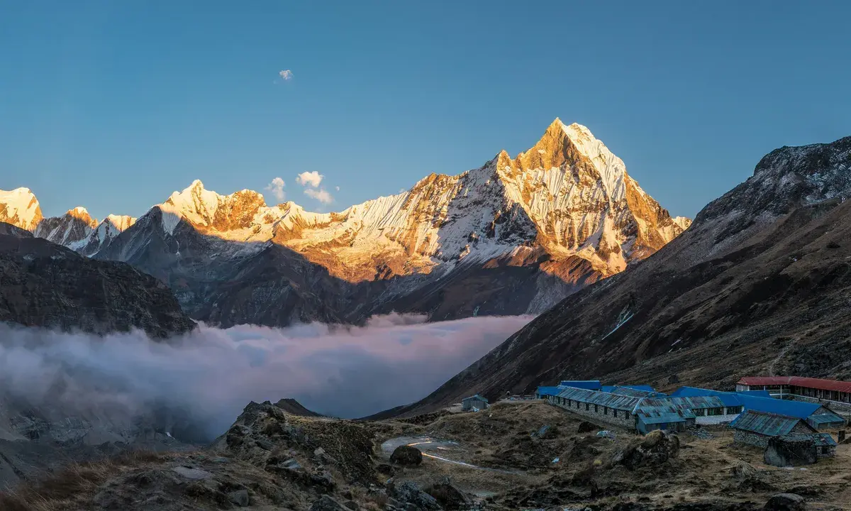 Golden sunrise alpenglow illuminating snow-capped Annapurna peaks above a sea of clouds with a teahouse lodge nestled in the 