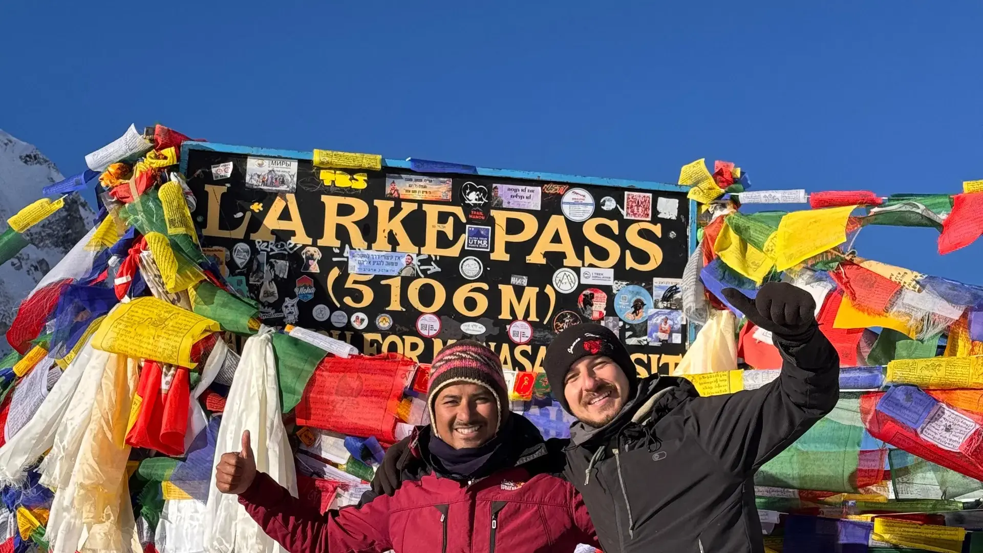 Two men celebrate at Larke Pass (5106m) amidst prayer flags in the Himalayas.