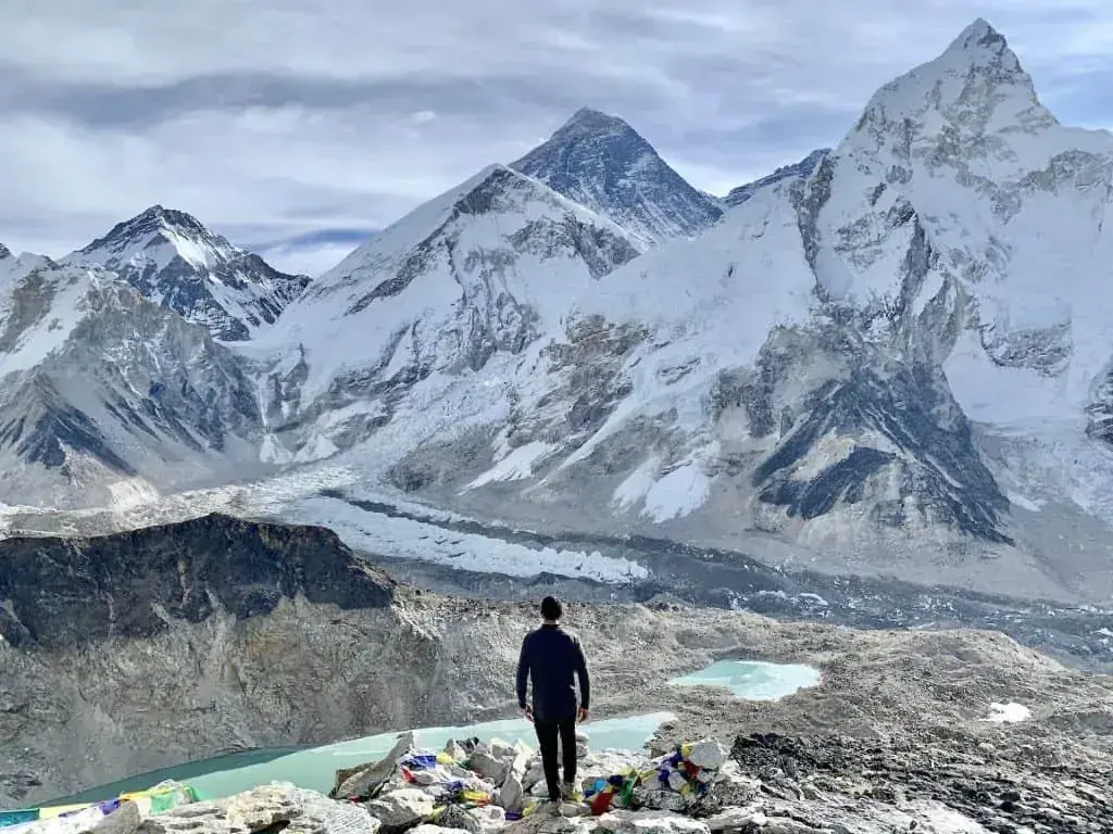 Man overlooking Everest, glacial lakes, and prayer flags.