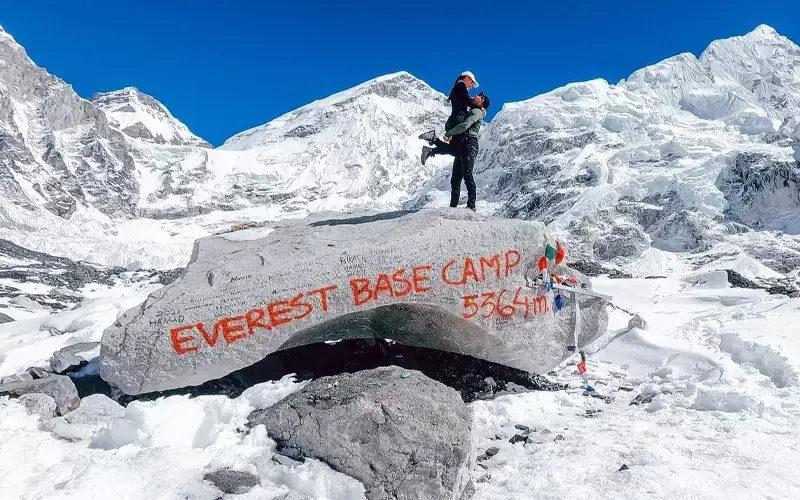 Couple embraces at Everest Base Camp, 5364m, with snowy peaks.