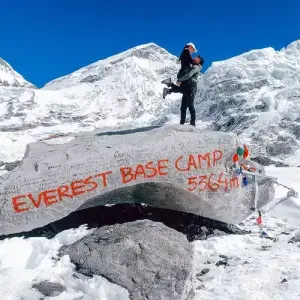 Couple embraces at Everest Base Camp, 5364m, with snowy peaks.