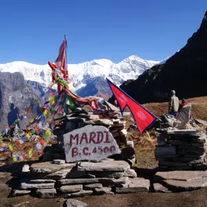 Mardi Himal Base Camp sign at 4500m with colorful prayer flags and snow-capped Himalayas in the background