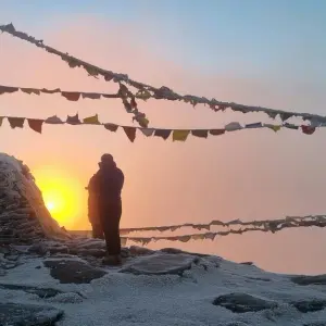 Silhouette of trekker at golden sunset with prayer flags and Himalayan horizon on Pikey Peak Trek, eastern Nepal