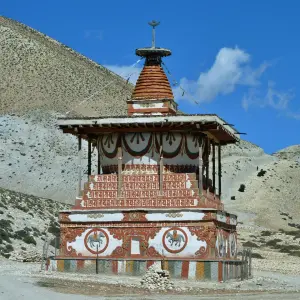 Ancient Buddhist chorten (stupa) with whitewashed walls and colorful decorations against arid rocky mountains in Upper Mustang, Nepal