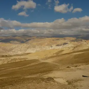 Lone trekker walking across vast golden arid plateau with dramatic cloudy sky in Upper Mustang, Nepal