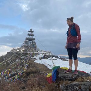 Trail runner standing at Ama Yangri Peak summit with snow and prayer flag monastery Nepal
