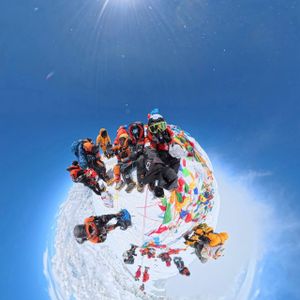 Climbers at the summit of Mount Everest surrounded by colorful prayer flags, captured in a 360-degree fisheye shot during the May 2026 expedition
