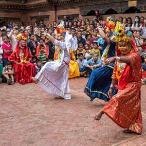 Lakhey in colourful costumes with floral headdresses performing traditional Nepali folk dance before a large crowd in a temple courtyard in Nepal